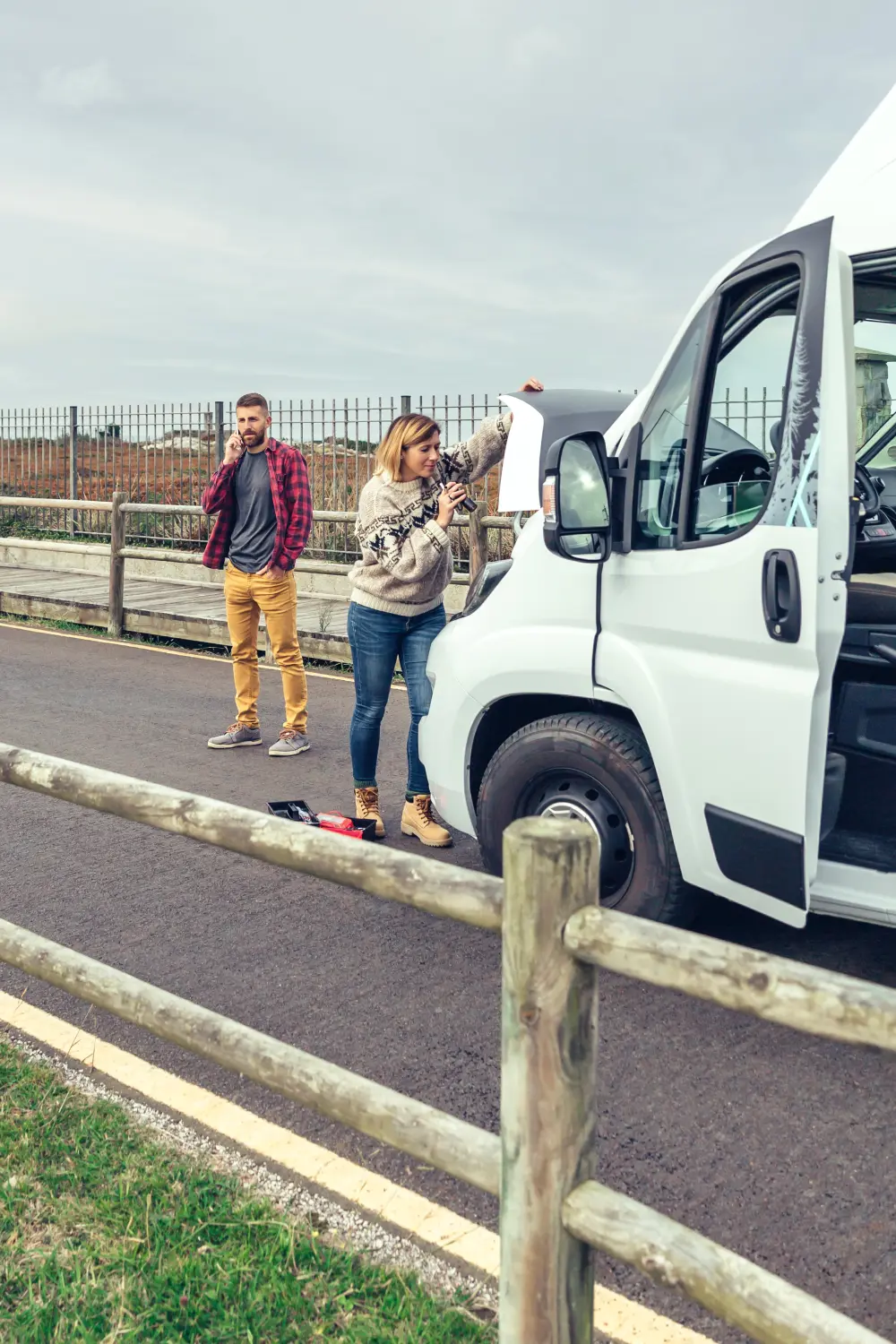 Frau wartet Wohnmobil mit Laterne und Werkzeug, während ihr Mann wartet.